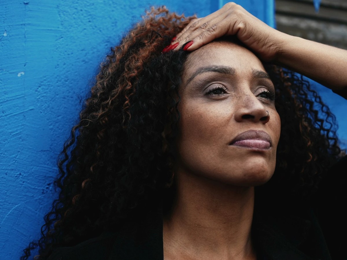 Frau steht vor einer blauen Wand und blickt ernst