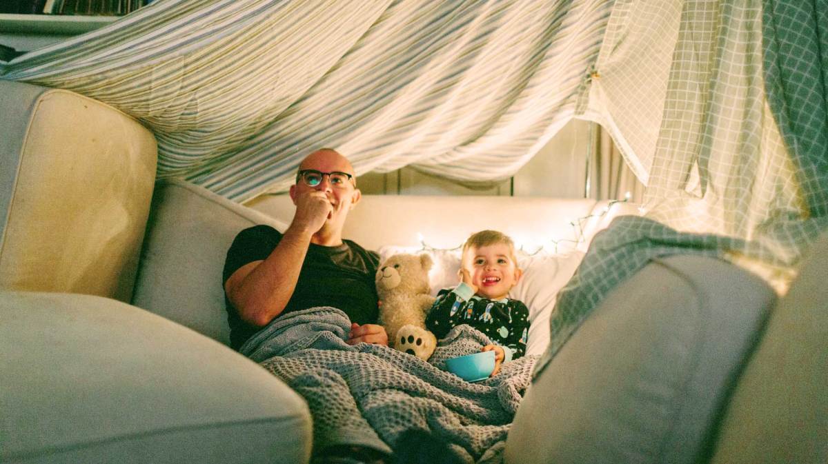 Vater und Sohn in einer selbstgebauten Höhle schauen einen Film und essen Popcorn.