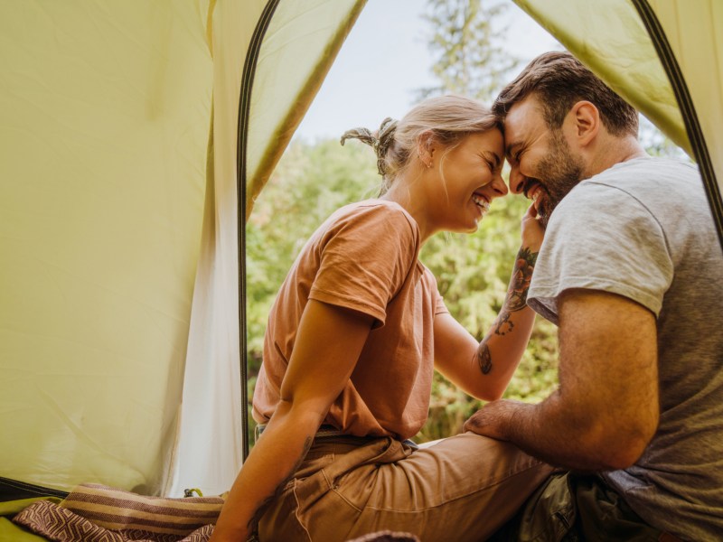 Frau und Mann in einem Zelt in der Natur, die sich anlächeln und sich mit der Stirn berühren