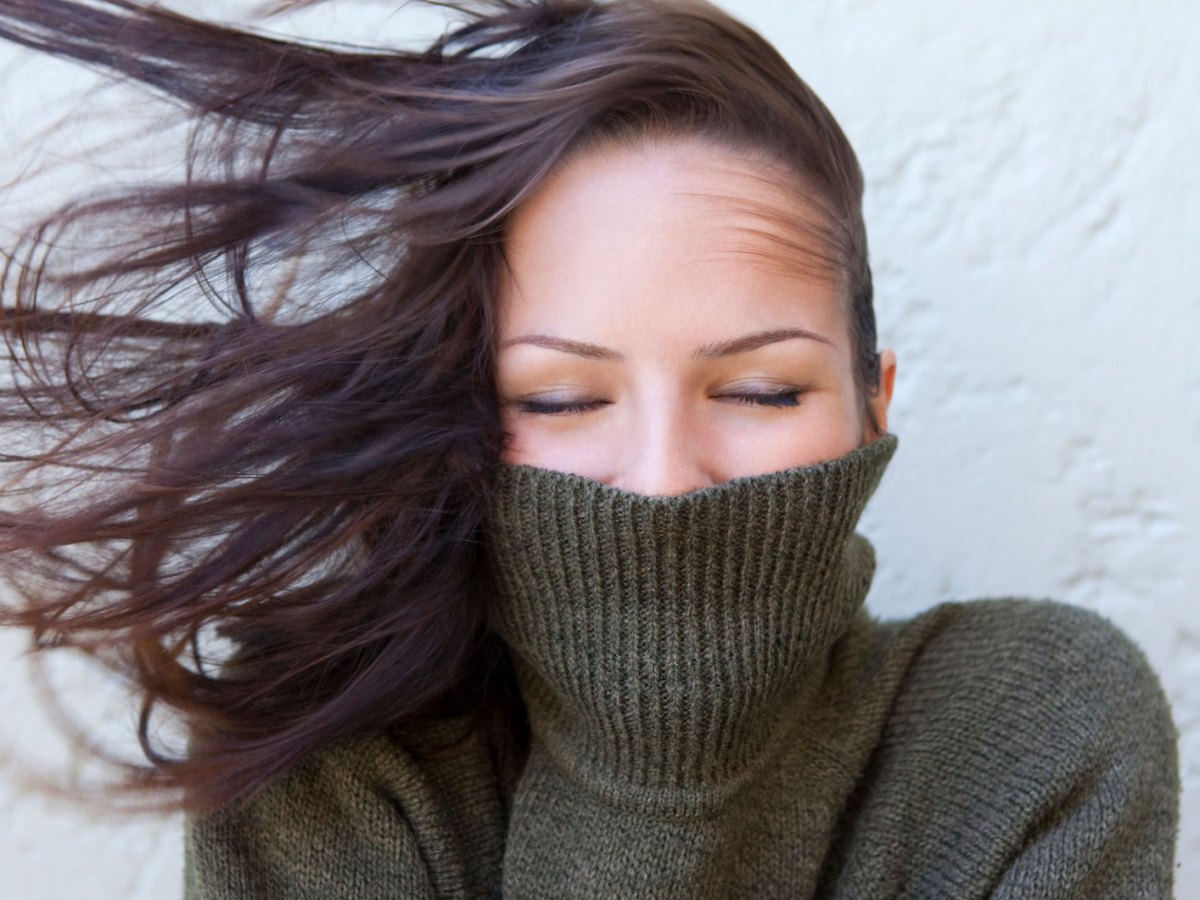 Frau mit einem Rollkragenpullover in dem sie ihr Gesicht versteckt