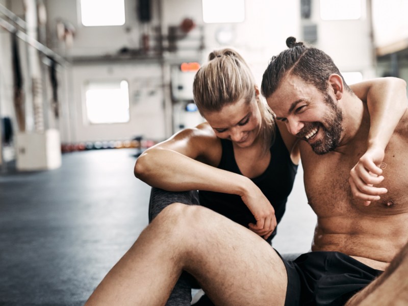 Ein Mann und eine Frau, die sich im Fitnessstudio in den Armen liegen und lachen