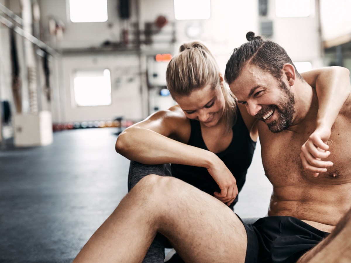 Ein Mann und eine Frau, die sich im Fitnessstudio in den Armen liegen und lachen