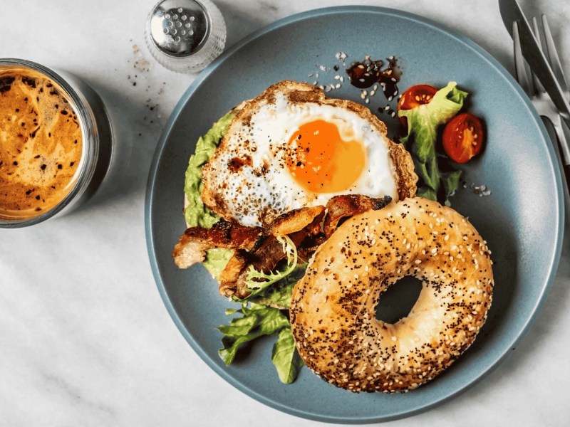 Bagel-Sandwich mit Avocado, Spiegelei und Beilagensalat und Kaffee auf weißem Hintergrund