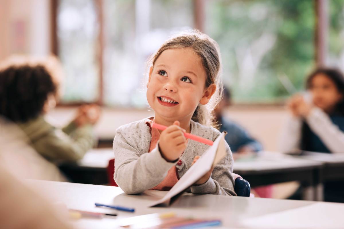 Schulanfängerin sitzt in der Klasse und zeigt etwas auf ihrem Block.