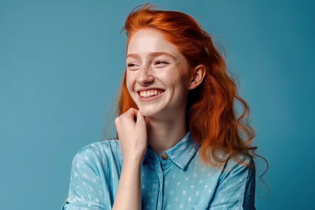Frau mit roten Haaren steht vor einer blauen Wand und lächelt