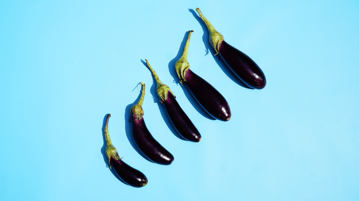 Fünf längliche lilafarbene Auberginen mit grünen Stielen liegen in einer diagonalen Linie auf hellblauem Hintergrund.