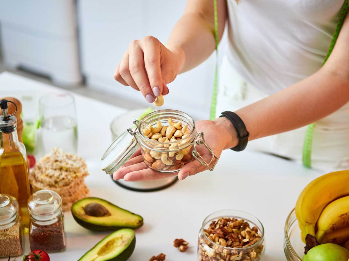 Junge glückliche Frau isst verschiedene Nüsse (Cashew, Haselnuss, Mandel) in der modernen Küche. Gesunde Ernährung und Diät-Konzept. Gewicht zu verlieren