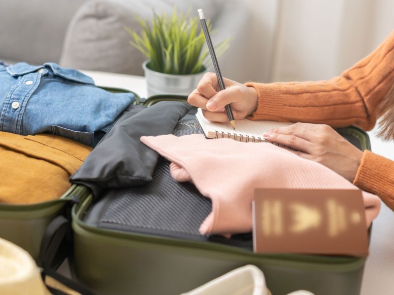 Frau erstellt Packliste für Urlaub auf gepacktem Koffer
