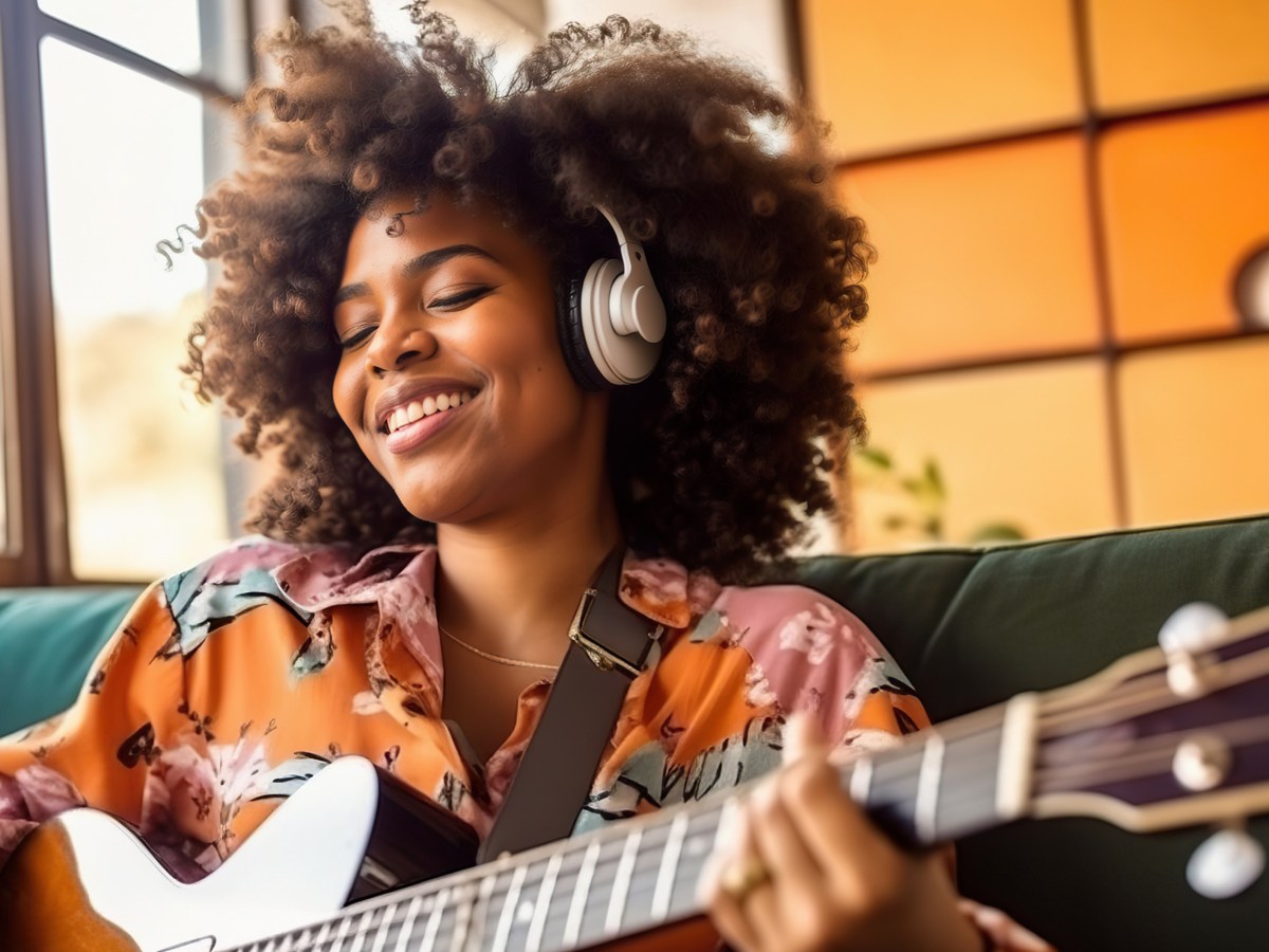 Afro-amerikanische Frau mit Gitarre in der Hand und Kopfhörern auf, die glücklich und entspannt auf einem Sofa sitzt