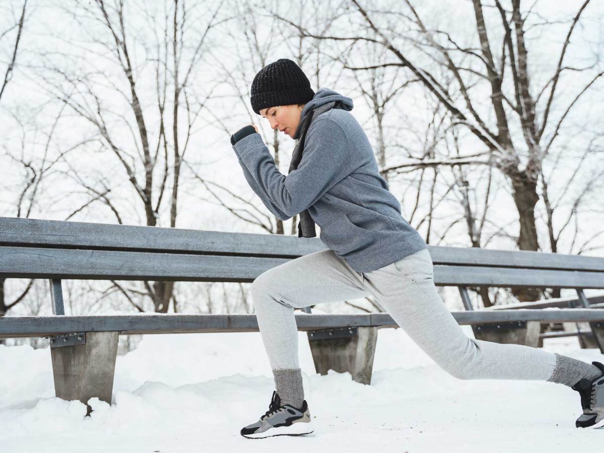 Sportliche Frau beim Aufwärmen vor ihrem Jogging-Training an einem verschneiten Wintertag in einem Stadtpark