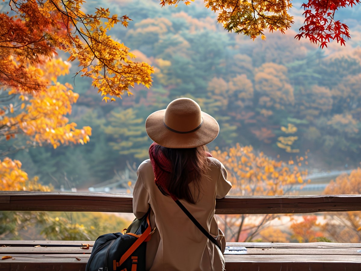 Frau mit Hut sitzt auf einer Bank unter herbstlichen Bäumen