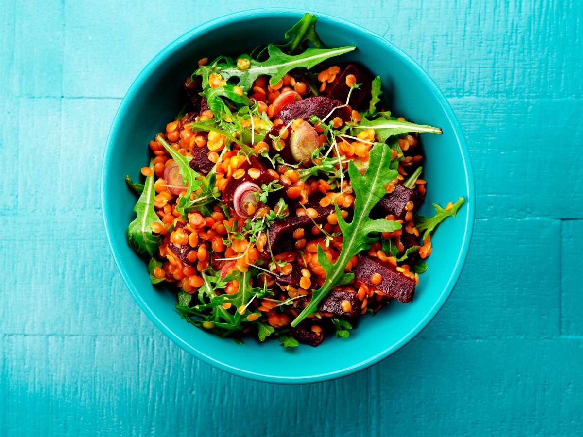 T&uuml;rkise Schale mit gesundem Salat aus Linsen, Rote Beete und Rucola, angerichtet auf blauem Holztisch.