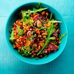Türkise Schale mit gesundem Salat aus Linsen, Rote Beete und Rucola, angerichtet auf blauem Holztisch.