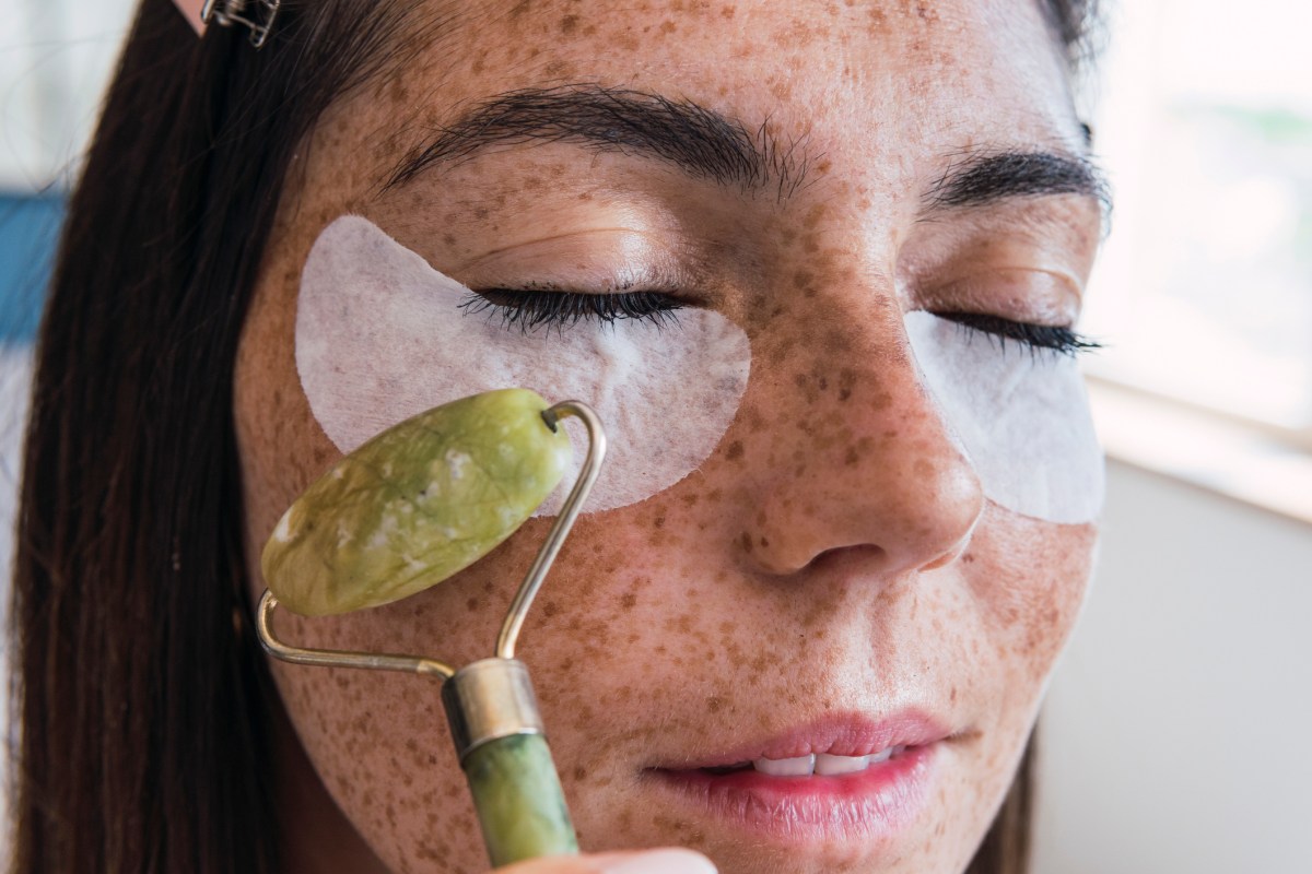Frau mit Augenpads und Jaderoller um Augenringe zu entfernen