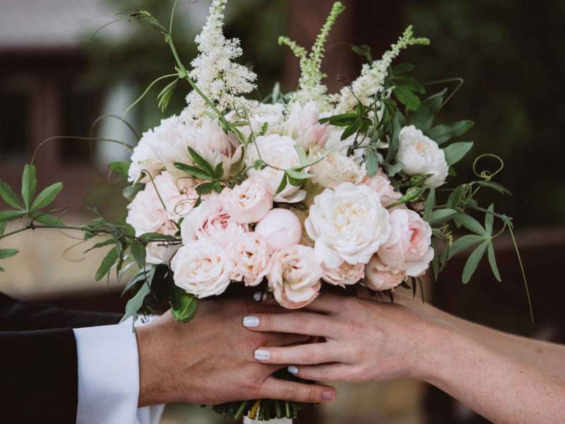 Frau und Mann halten gemeinsam einen Brautstrauß mit vielen Rosen.