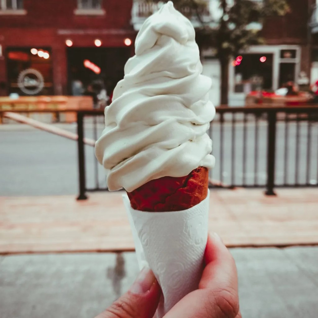 Luftzeichen: Frozen Yoghurt und Softeis Softeis in der Hand einer Frau im Hörnchen.
