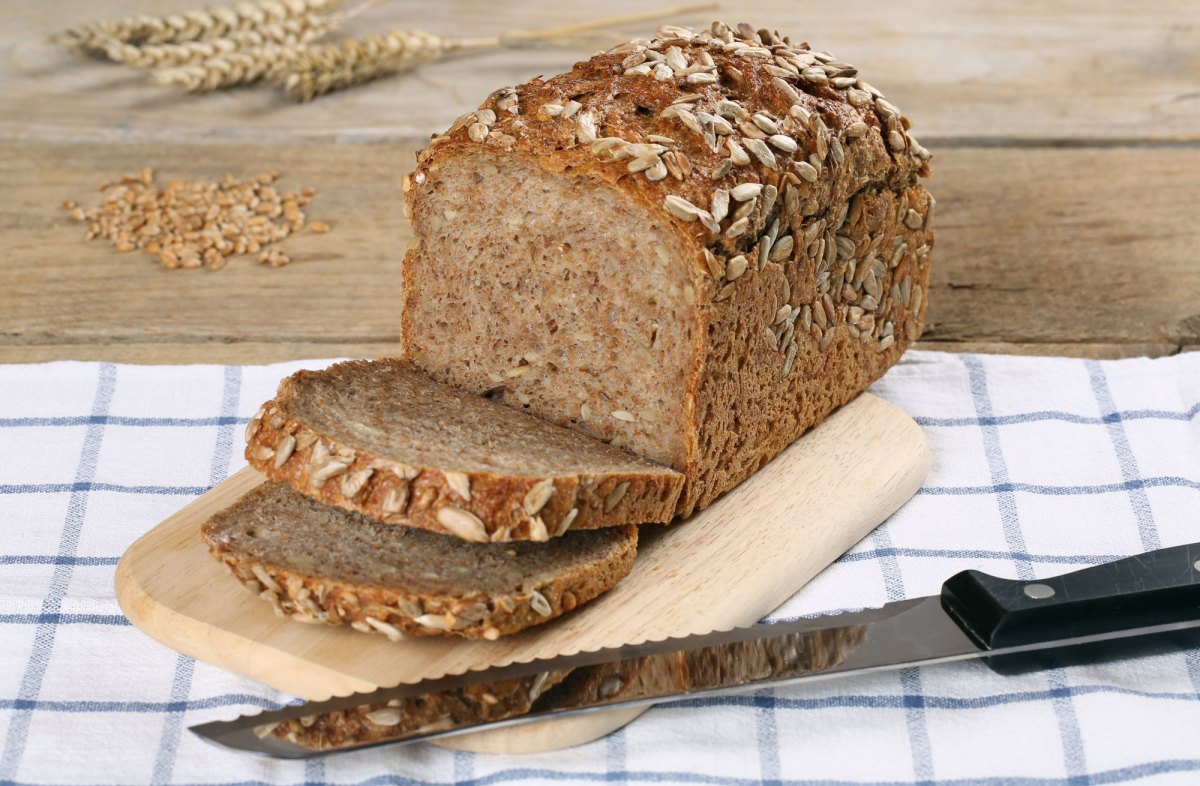 Vollkornbrot im Anschnitt auf Holzbrett, davor Messer