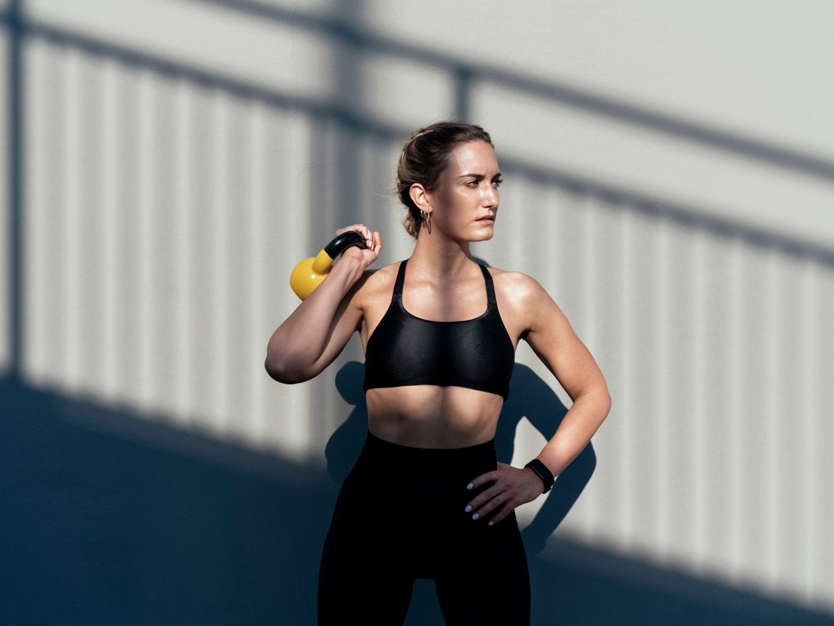 Krafttraining Frauen: Trainierte Frau in Sport-BH und Leggings mit gelber Kettlebell vor Wand