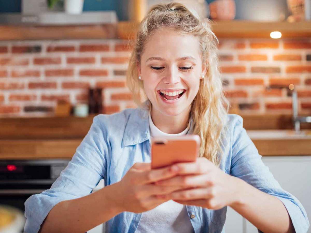 Junge blonde Frau sitzt an ihrem Handy.