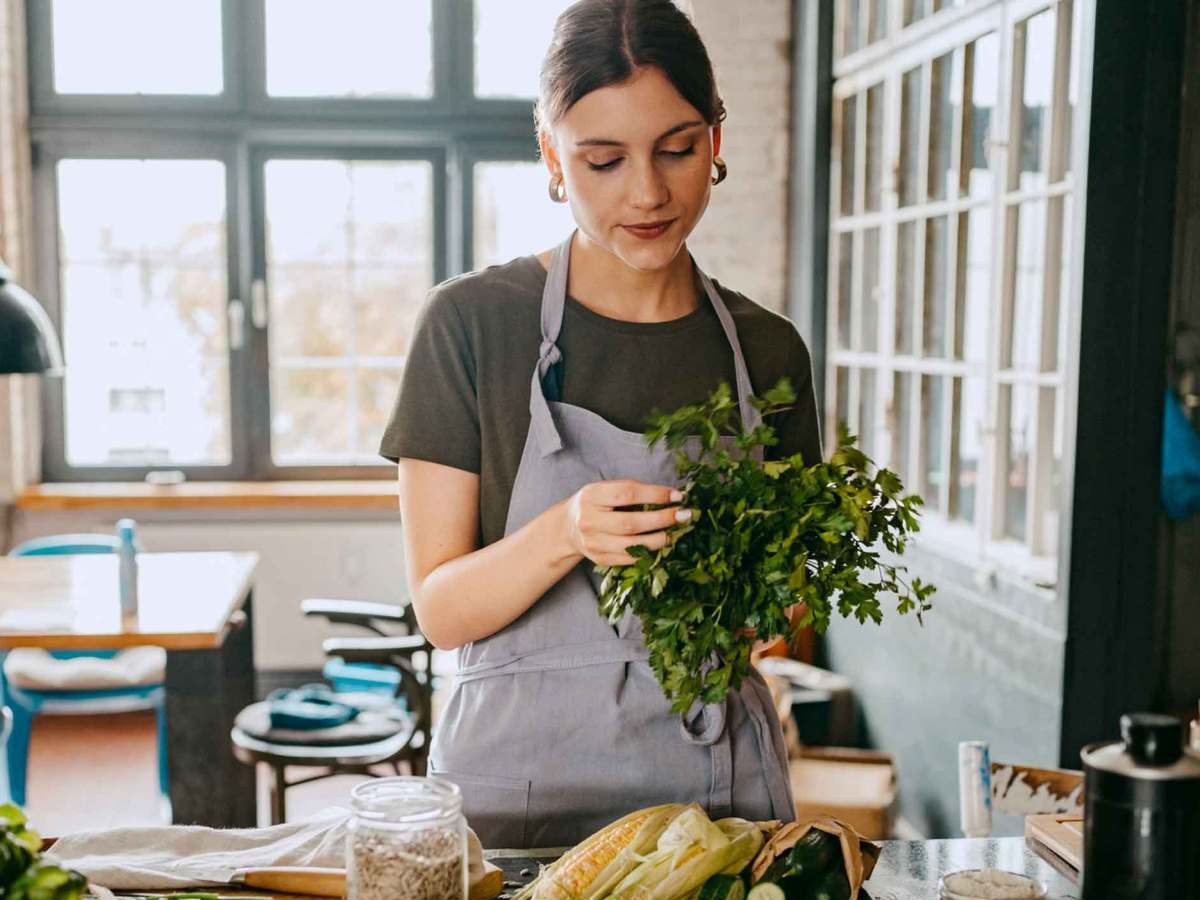 Eine Frau kocht in ihrer Küche und zupft Kräuter.