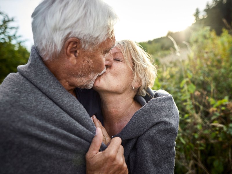 Älteres Paar küsst sich auf einer Wiese