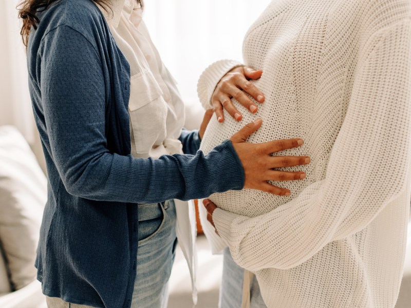 Symbolbild für Leihmutter: Eine Frau legt Hände auf den Babybauch einer anderen Frau