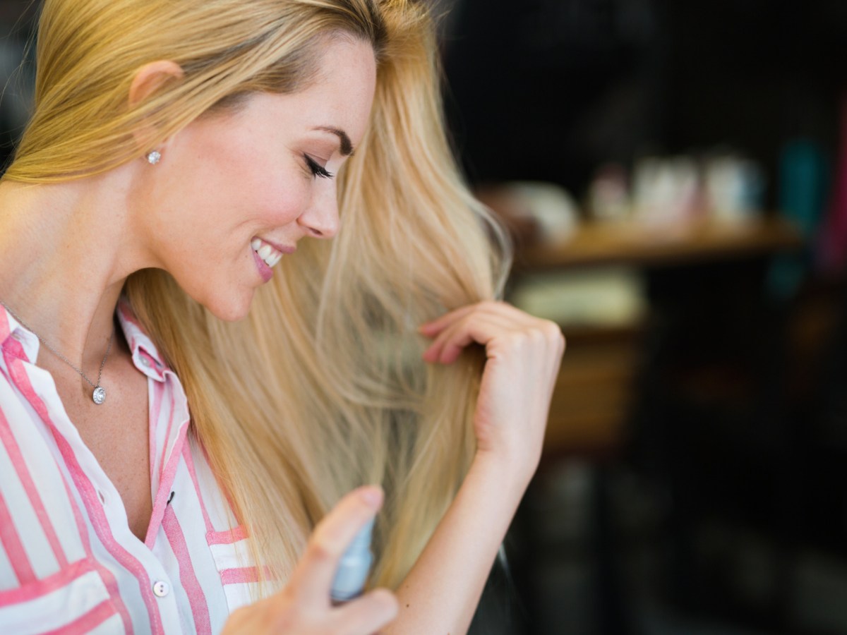 Eine blonde Frau spr&uuml;ht sich Parfum in die Haare