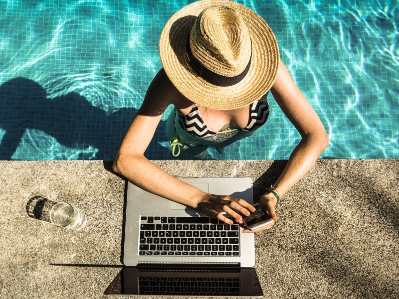 Frau mit Sonnenhut und Laptop am Pool