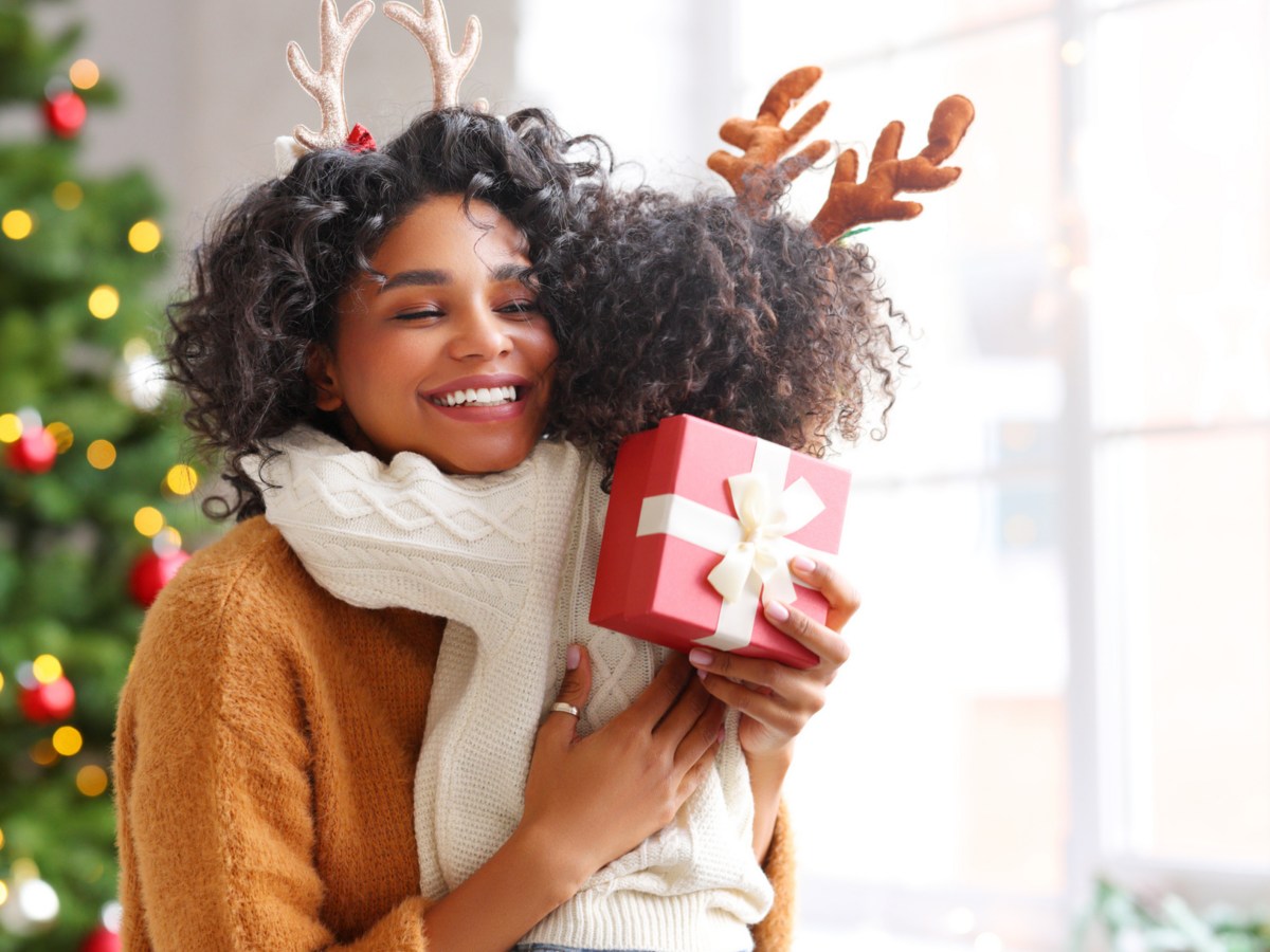 Mutter und Kind umarmen sich vor einem Weihnachtsbaum und &uuml;bergeben ein Geschenk.