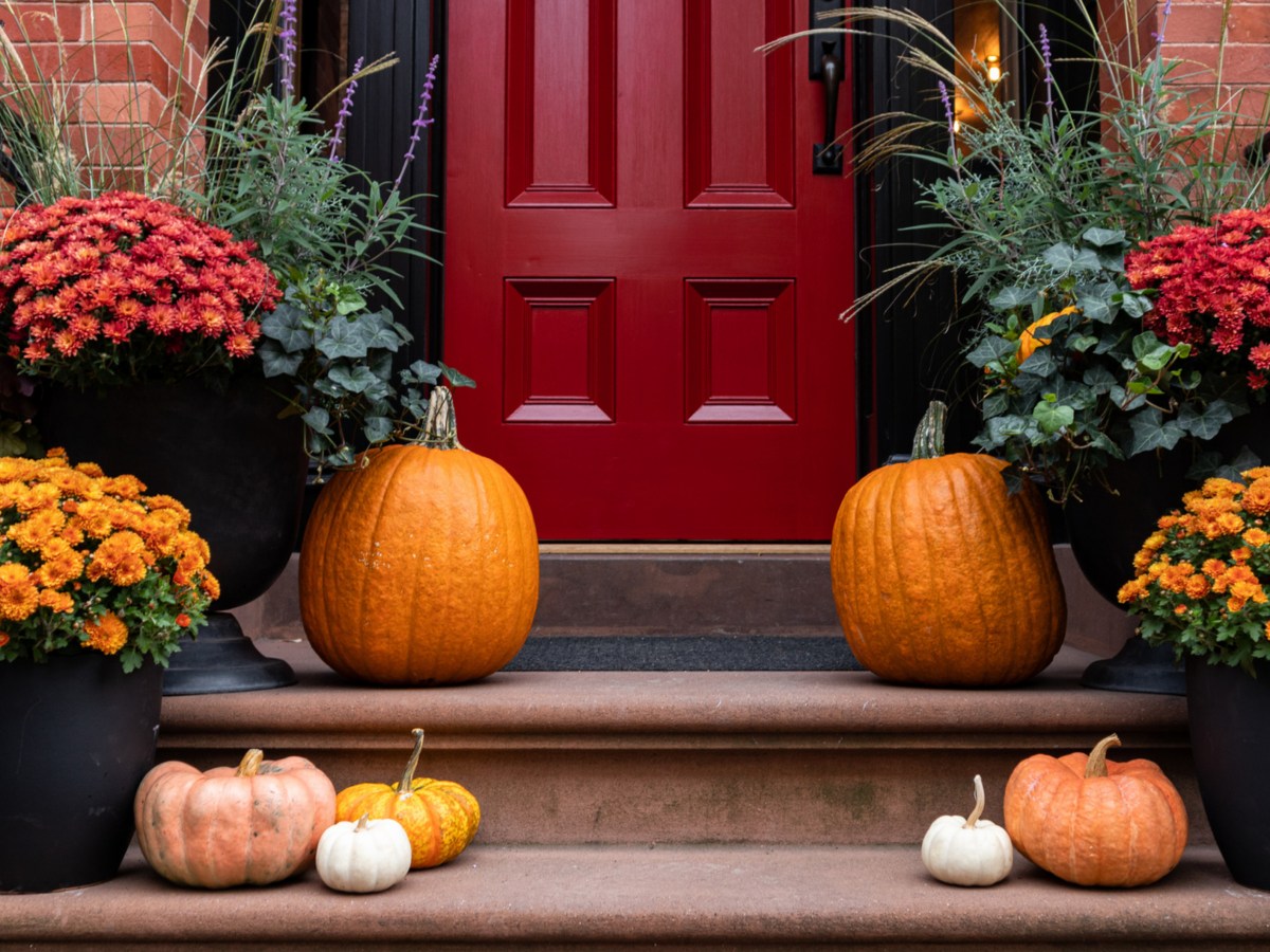 Hauseingang mit roter Tür, davor stehen Kürbisse als Herbstdeko.