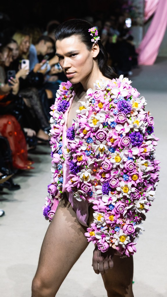 Ein Model in einem einzigartigen, mit LEGO Botoncials Blumen besetzten Mantel und passendem Haarschmuck läuft über den Laufsteg.