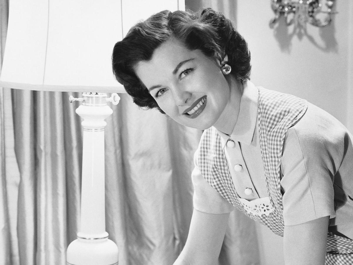 Bild einer Frau aus den 50/60er Jahren mit einer Hochsteckfrisur und einer Schürze. Sie wischt einen Tisch sauber.