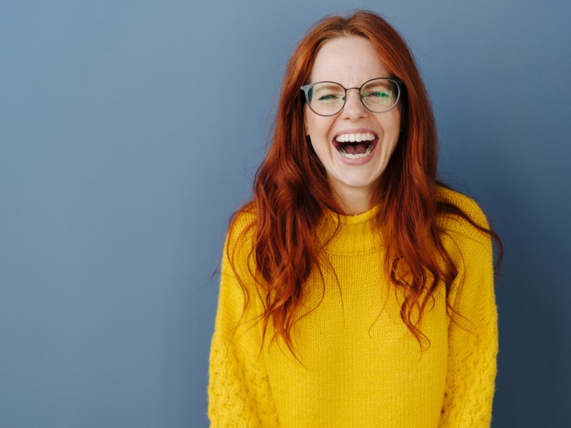 Lachende Frau mit roten Haaren und gelbem Pullover