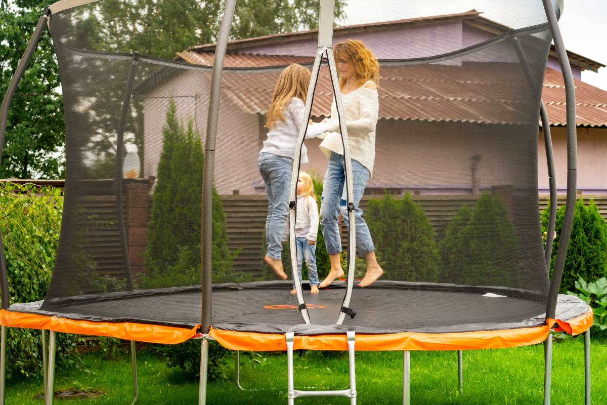 Mutter und Kinder springen gemeinsam auf ihrem Trampolin im eigenen Garten.