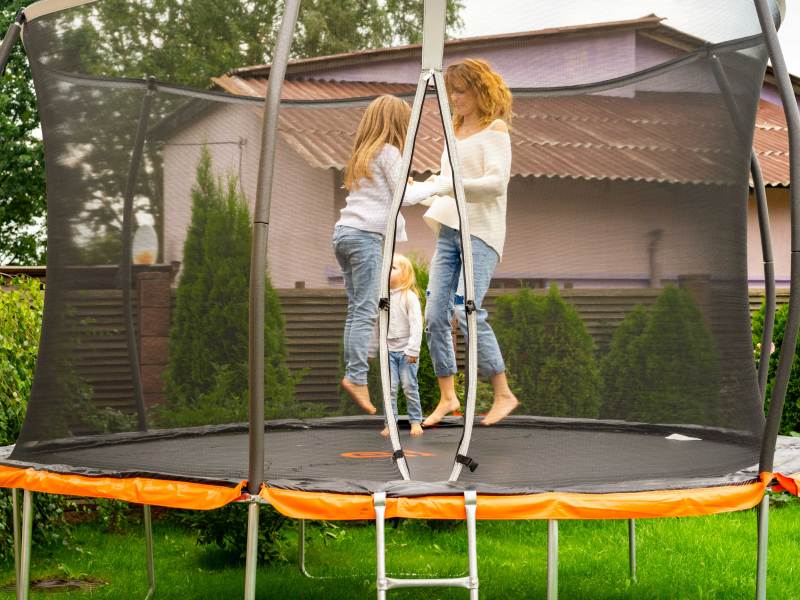 Mutter und Kinder springen gemeinsam auf ihrem Trampolin im eigenen Garten.