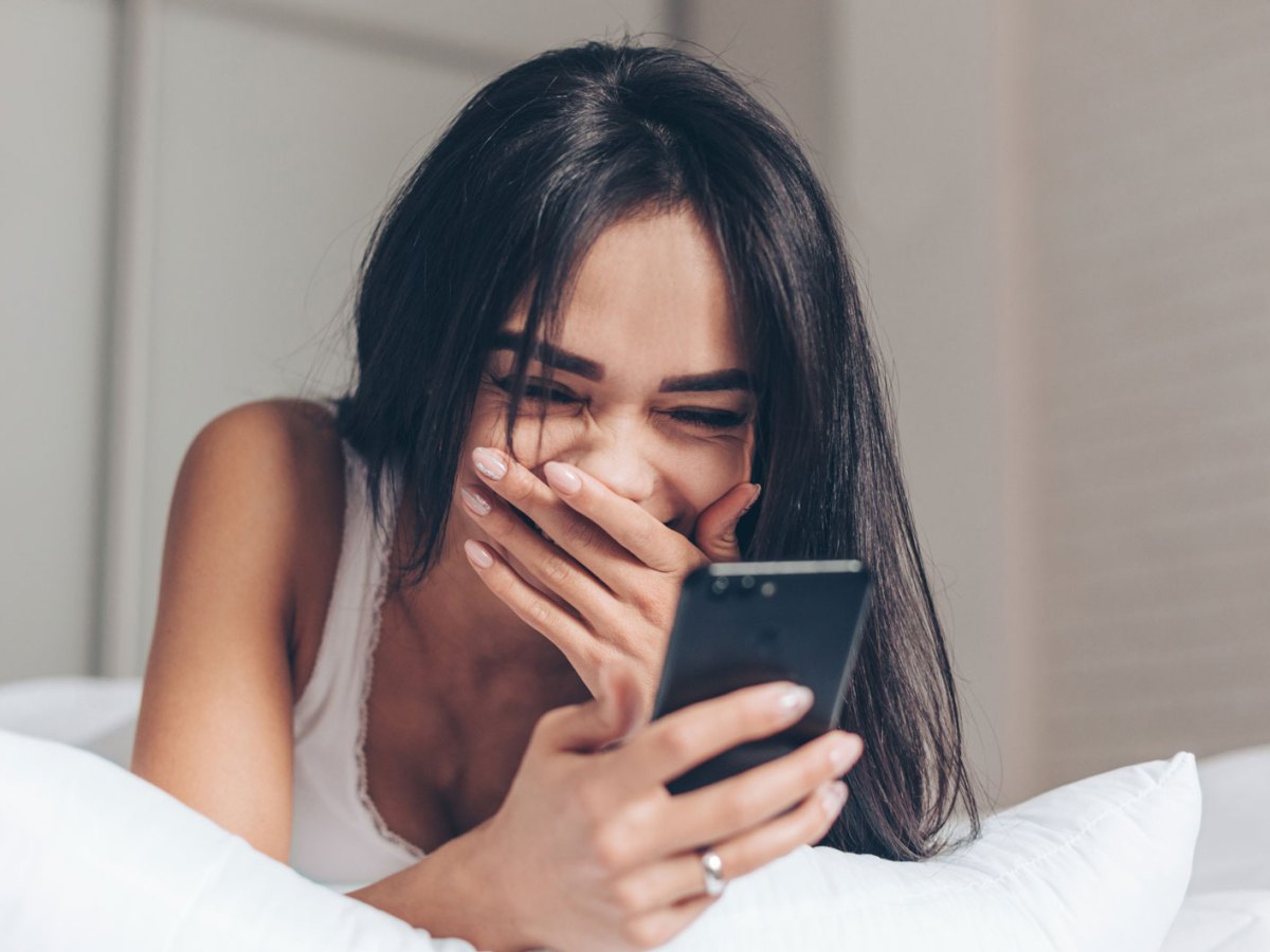 Frau schaut auf ihr Smartphone und lacht