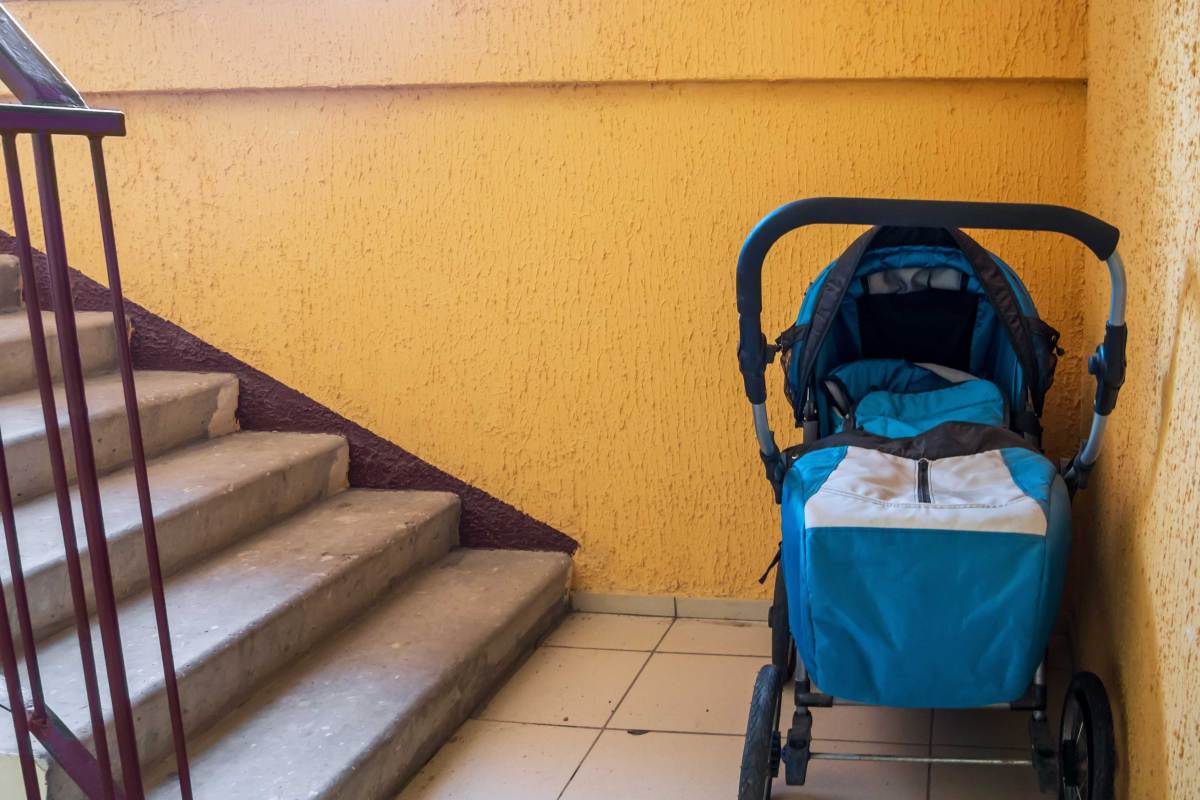 Bild eines Kinderwagens der am Fuße einer Treppe eines Wohnhauses steht.