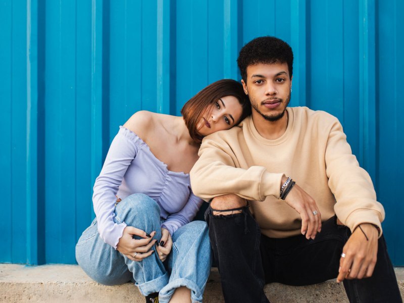 Mann und Frau sitzen ernst nebeneinander vor einer blauen Wand.