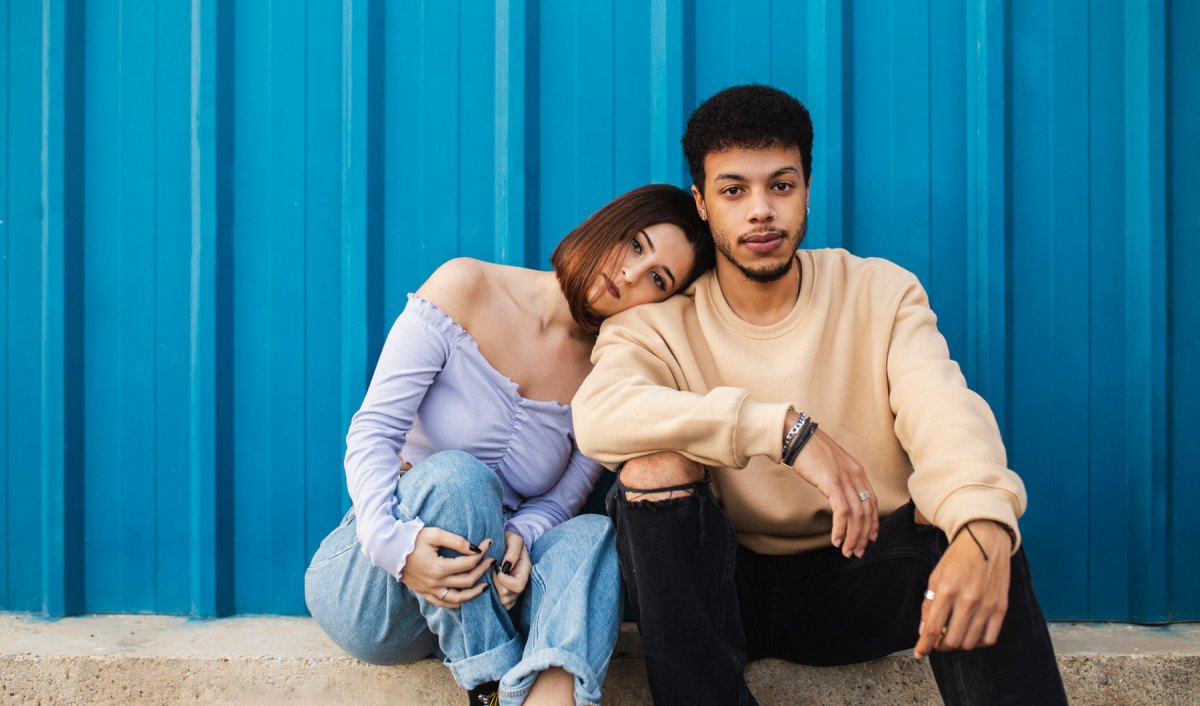 Mann und Frau sitzen ernst nebeneinander vor einer blauen Wand.