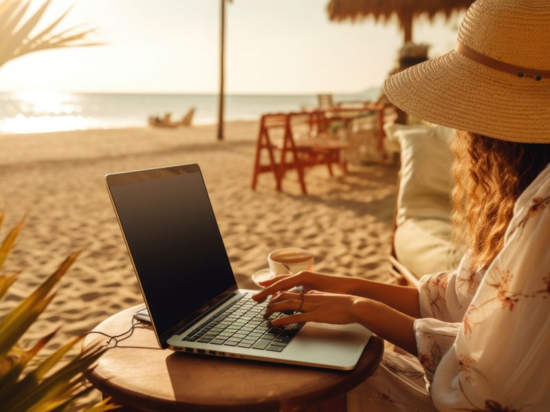Frau sitzt am Strand mit dem Laptop auf dem Schoß.