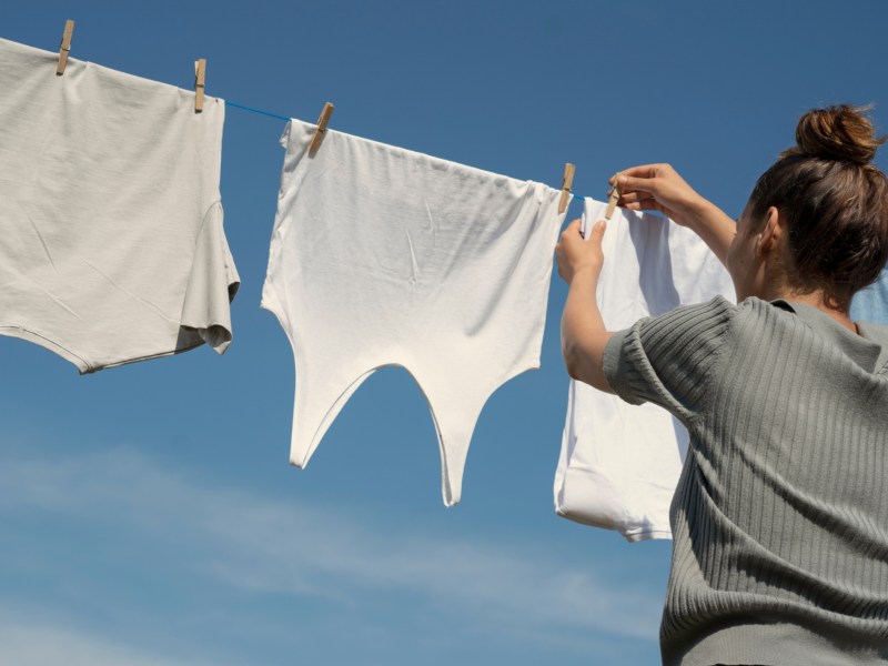 Eine Frau hängt weiße Kleidung auf eine Wäscheleine in die Sonne.