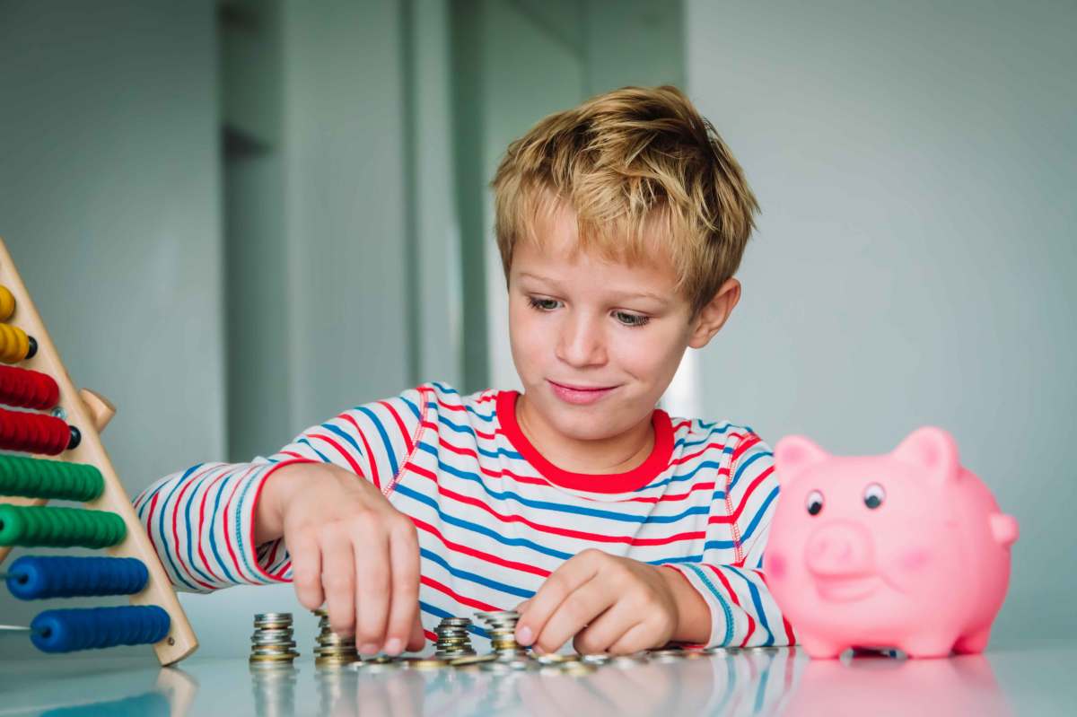 Junge, ca. 8 Jahre, zählt sein Taschengeld. Auf dem Tisch stehen außerdem ein Sparschwein und ein Rechenschieber.