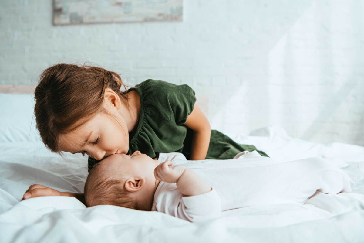 Große Schwester gibt ihrer kleinen Babyschwester einen Kuss auf die Stirn.