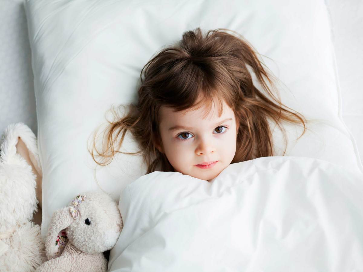 Zirka vierj&auml;hriges M&auml;dchen liegt zugedeckt und hellwach im Bett.