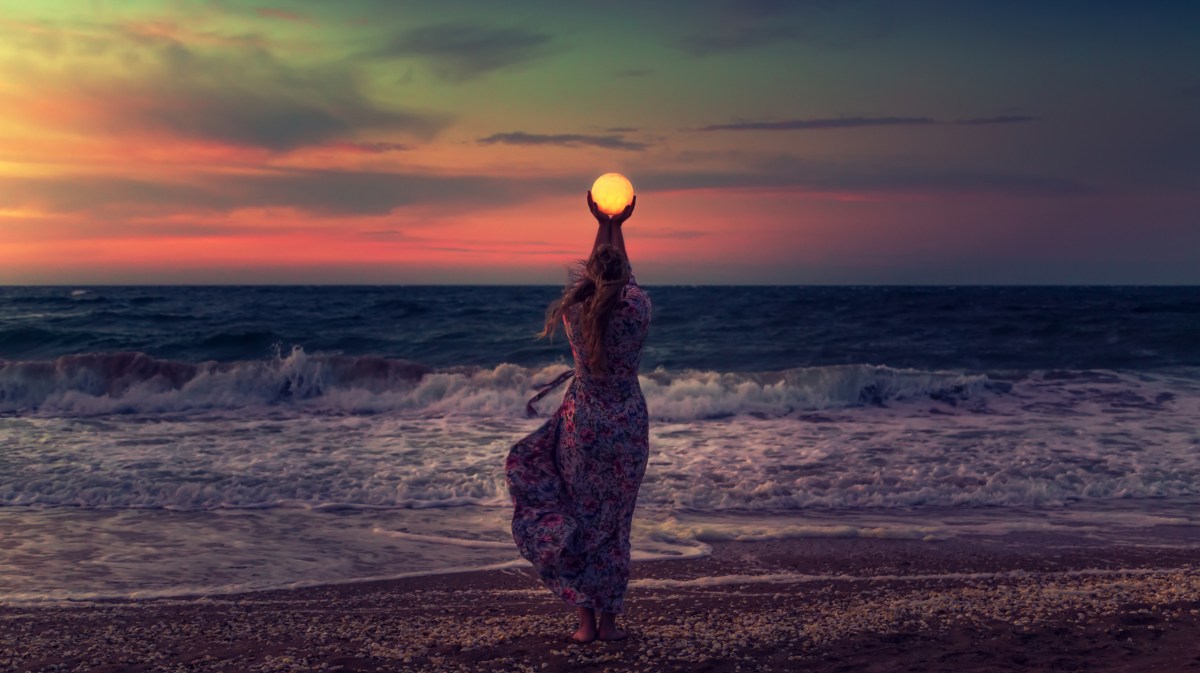 Frau am Strand, die mit ihren Händen den Mond in ihren Händen hält