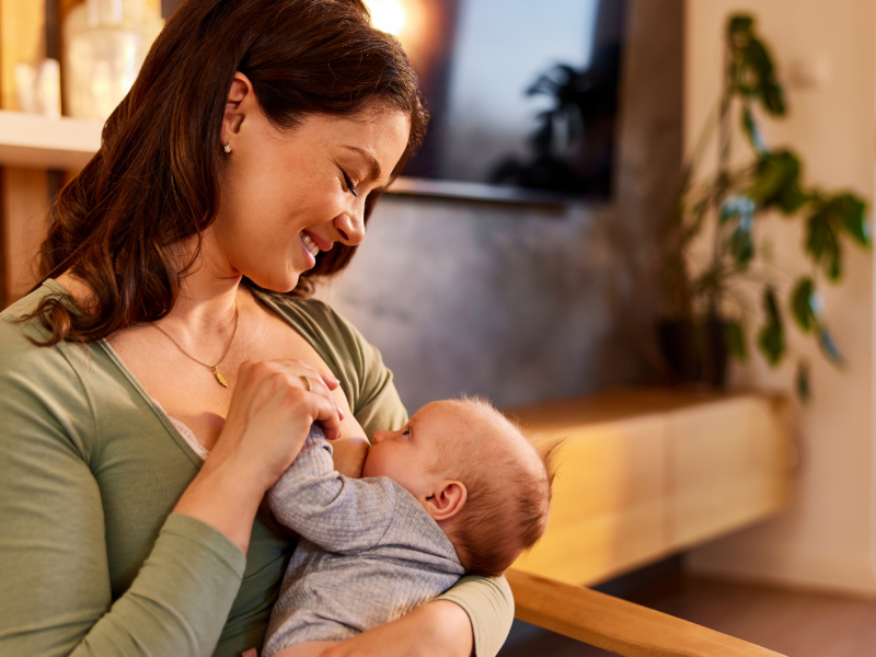 Junge Frau hält ihr Baby vor sich und stillt es