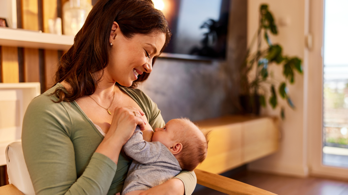 Junge Frau hält ihr Baby vor sich und stillt es