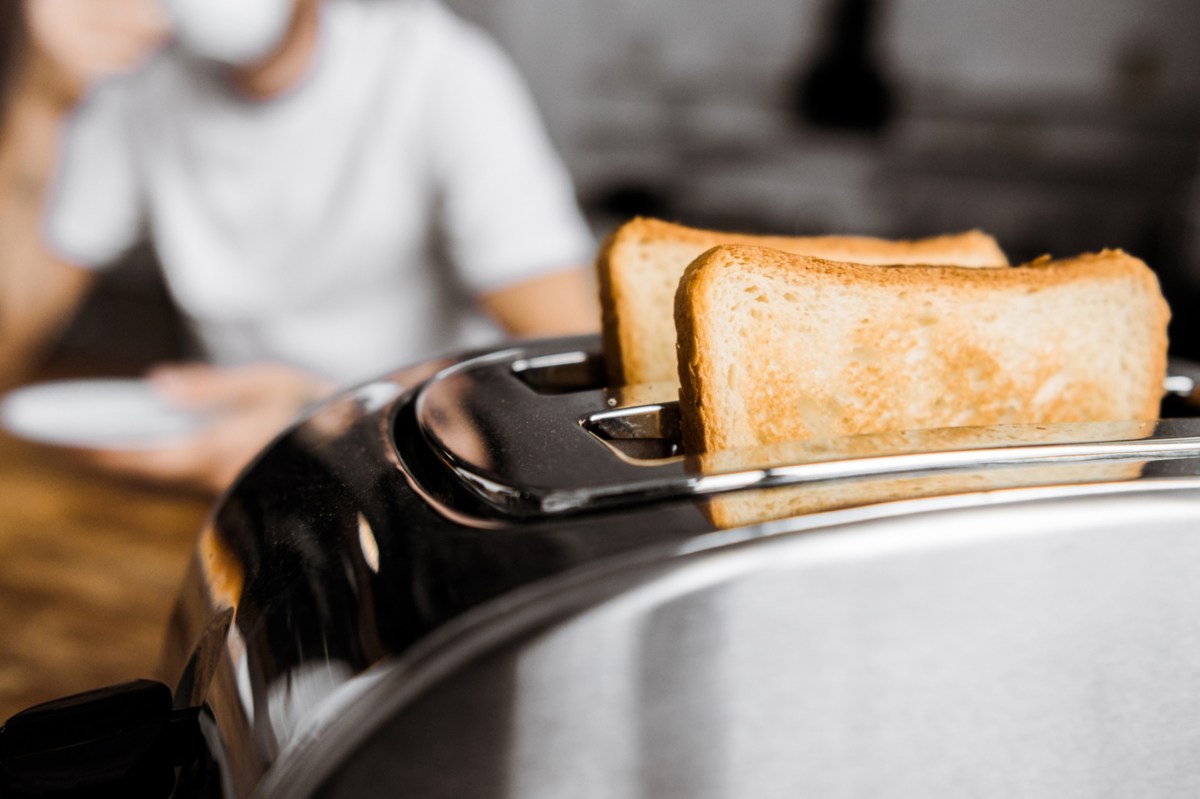 Ein Mann sitzt am Frühstückstisch. Im Vordergrund steht ein Toaster mit frisch getoasteten Brotscheiben.