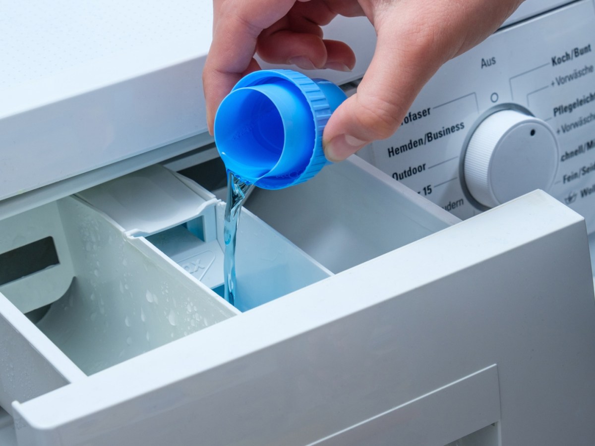 Person füllt flüssiges Waschmittel in Waschmaschinenfach.
