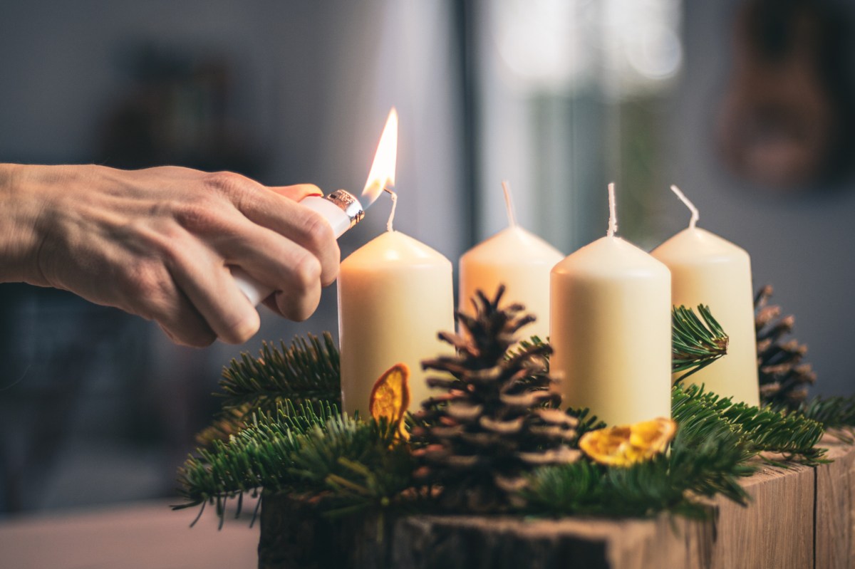 Eine Kerze auf einem Adventskranz wird mit einem Feuerzeug angezündet.